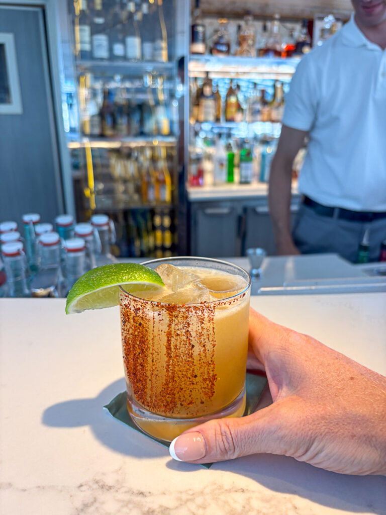 image of spicy margarita cocktail with tajin and lime on rim, at bar held by female hand with french manicure
