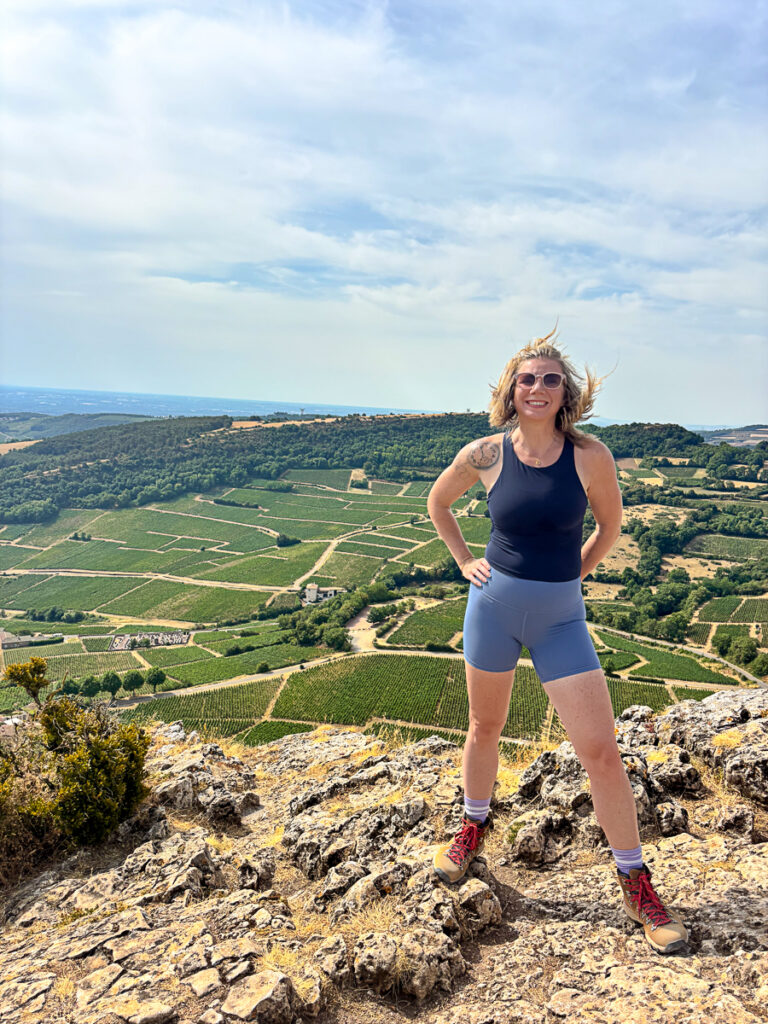female hiker posing at summit of rock or solutre with wind blowing hair and vineyards below in background